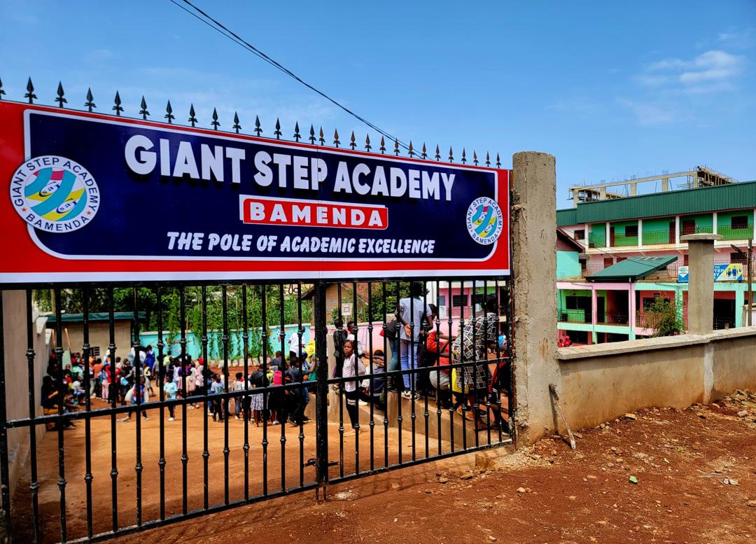 The Giant Step Academy Bamenda gate sign: The Pole of Academic Excellence, pupils in the schoolyard behind